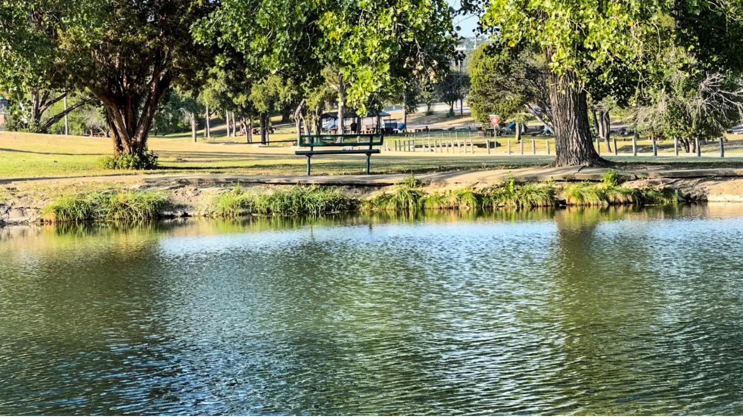 Peaceful park scene in Copperas Cove, TX, with a bench overlooking a reflective pond surrounded by trees and grass